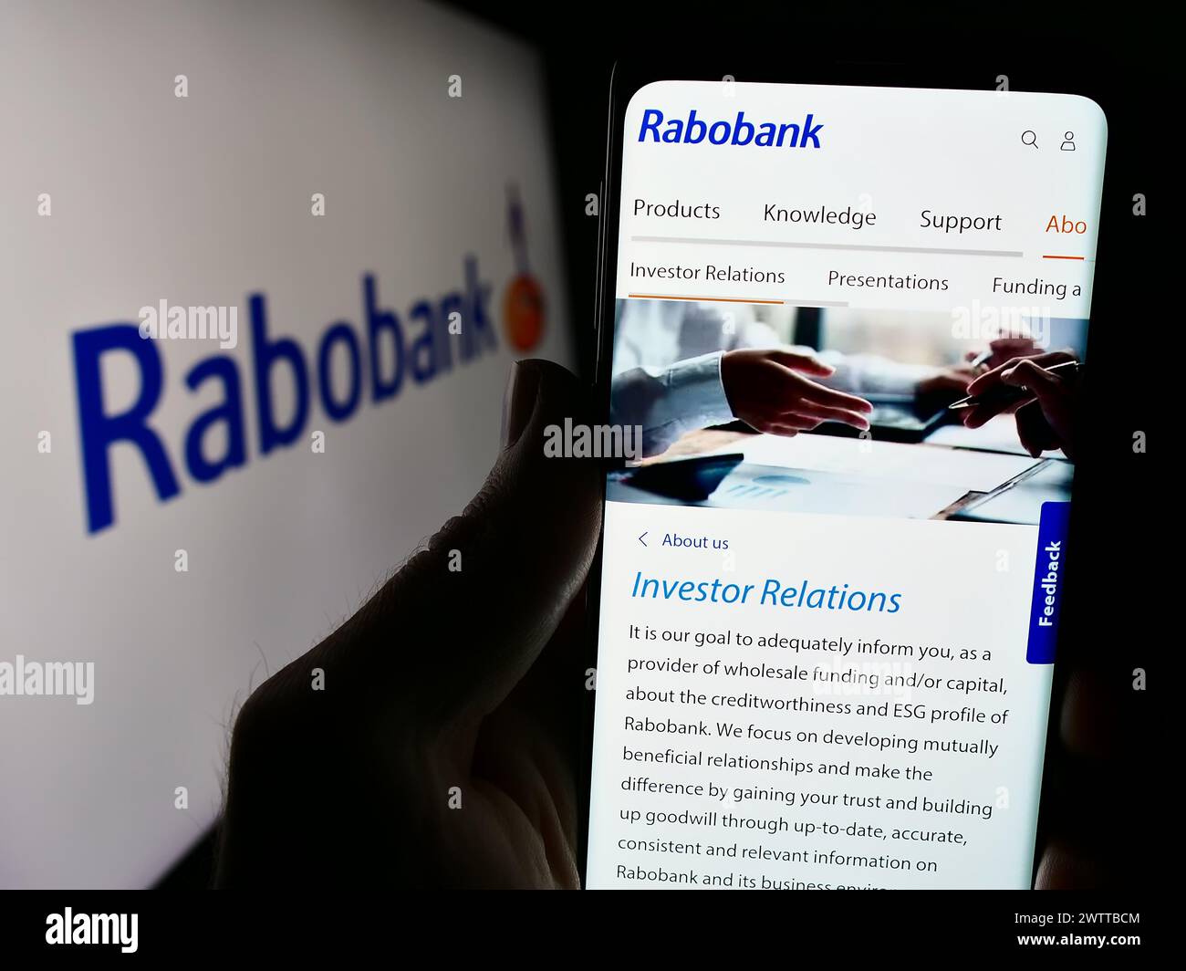 Persona che detiene un cellulare con pagina web della società bancaria olandese Cooperatieve Rabobank U.A. davanti al logo. Messa a fuoco al centro del display del telefono. Foto Stock