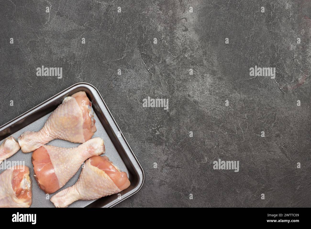 Cosce di pollo nel vassoio da forno in metallo Ramo verde di pomodoro sul tavolo. Sfondo nero. Copia spazio Foto Stock