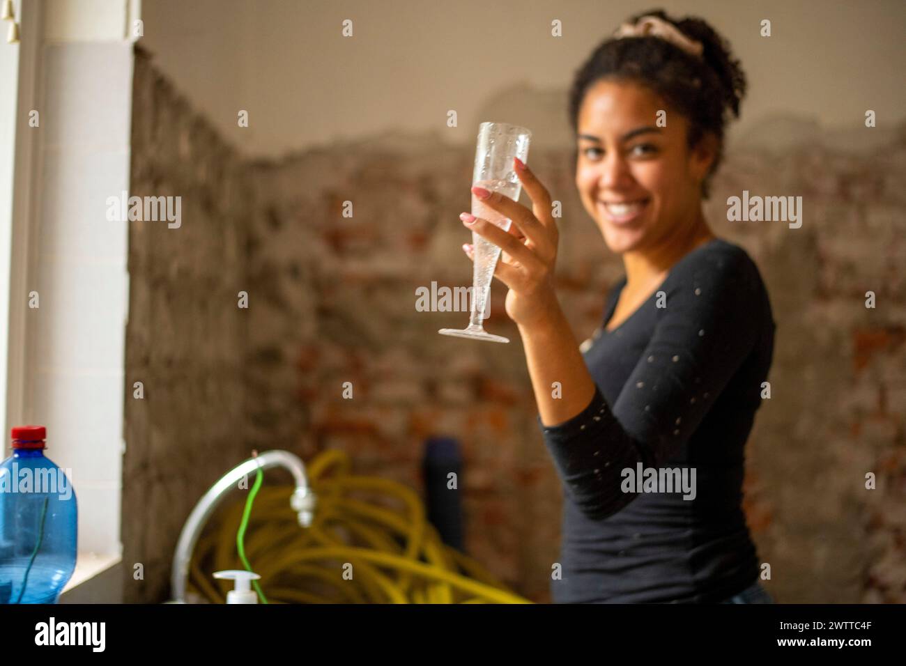 Giovane donna sorridente che tiene un bicchiere di champagne in una camera in fase di ristrutturazione Foto Stock