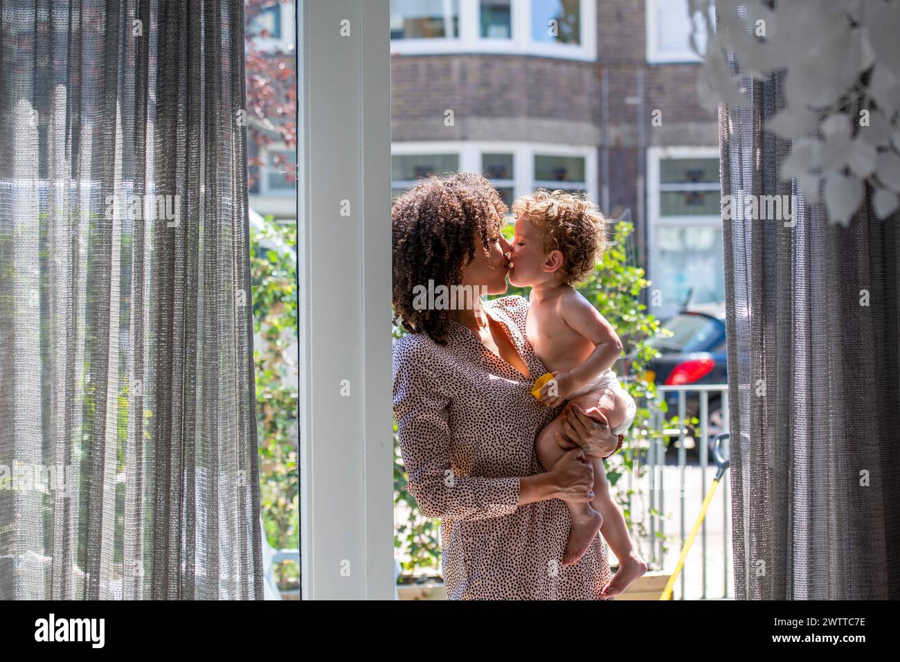 Madre e figlio condividono un abbraccio amorevole vicino a una finestra illuminata dal sole. Foto Stock