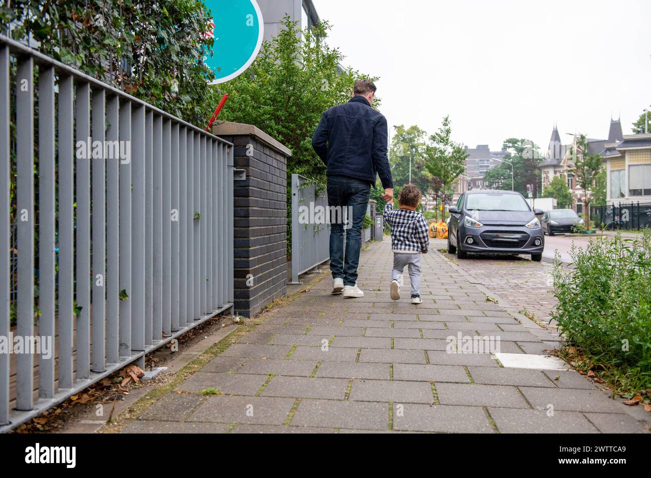 Un genitore e un bambino si godono una passeggiata in una tranquilla strada di periferia. Foto Stock