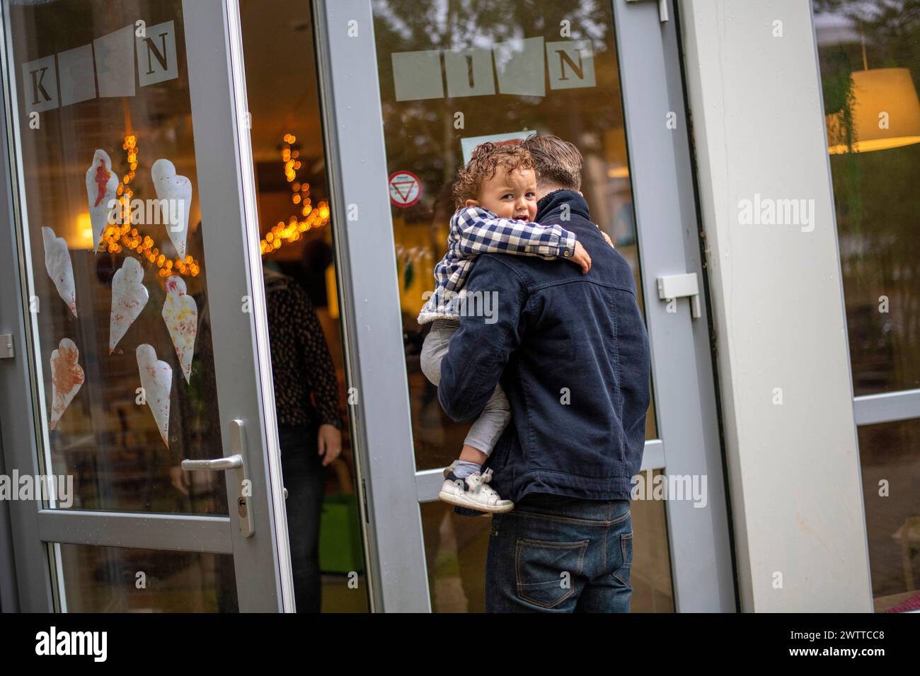 Un momento tenero quando un genitore abbraccia il proprio bambino vicino a un'accogliente entrata della caffetteria. Foto Stock