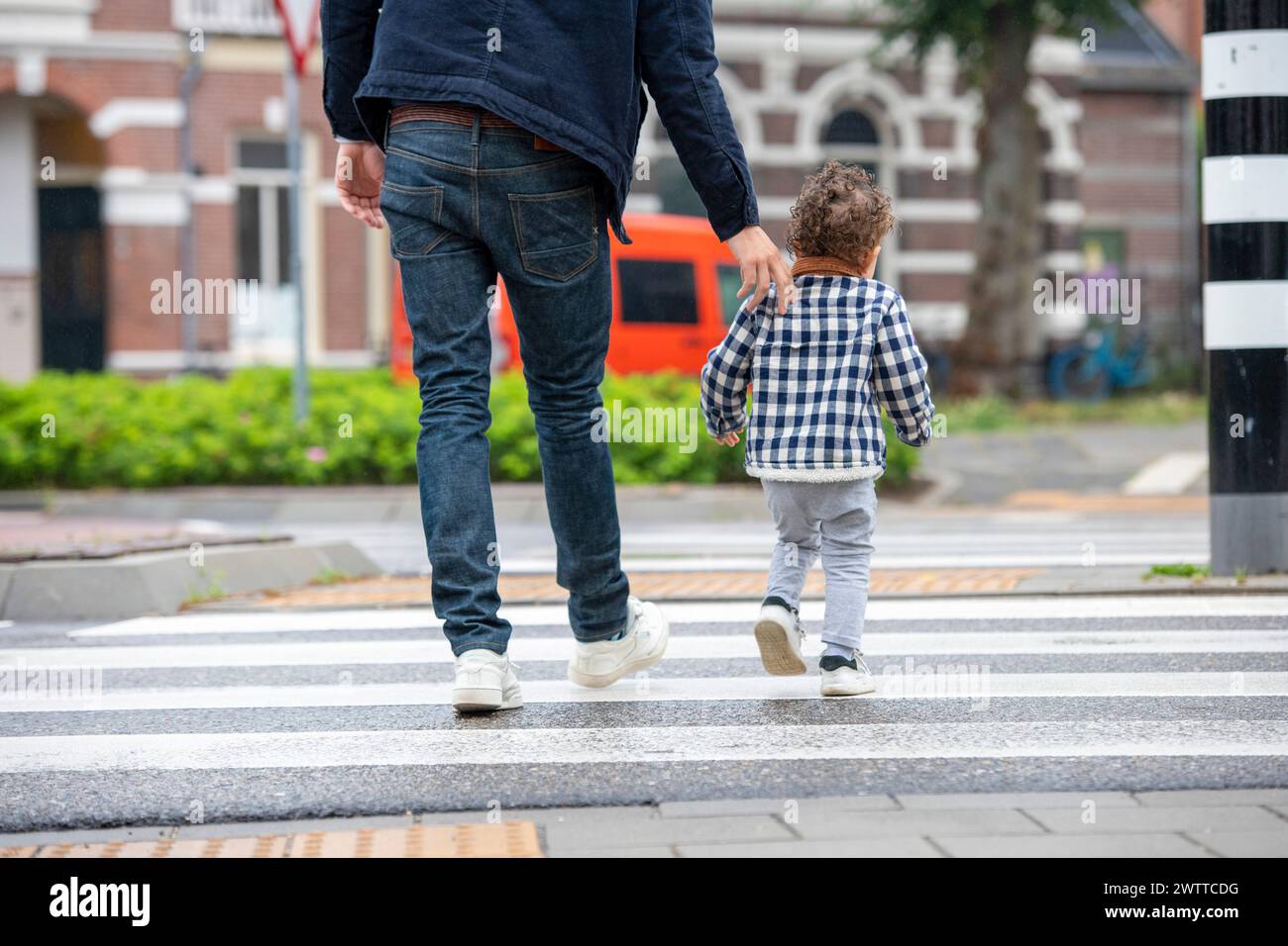 Un genitore e un bambino che si tengono per mano mentre attraversano la strada. Foto Stock
