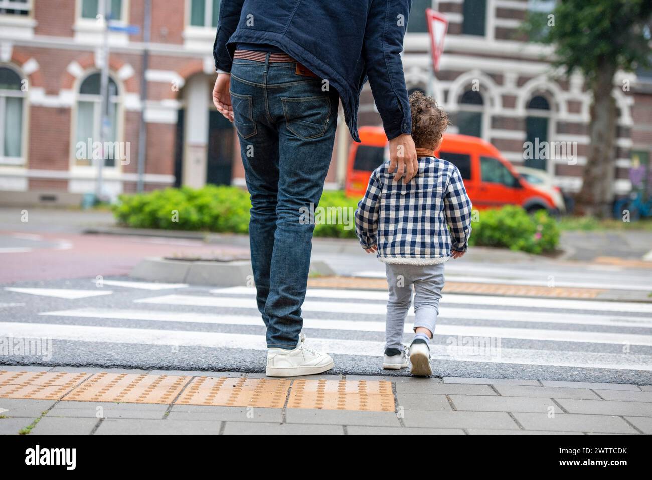 Un genitore e un bambino si tengono per mano mentre attraversano la strada in una giornata nuvolosa. Foto Stock
