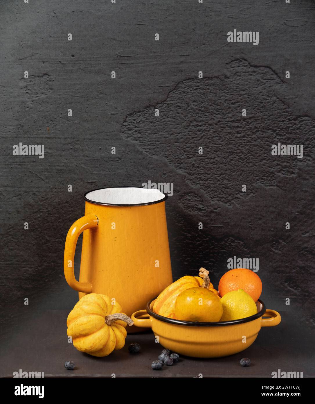 Un'accogliente natura morta autunnale con una tazza dai toni caldi e una ciotola con zucche e arance Foto Stock