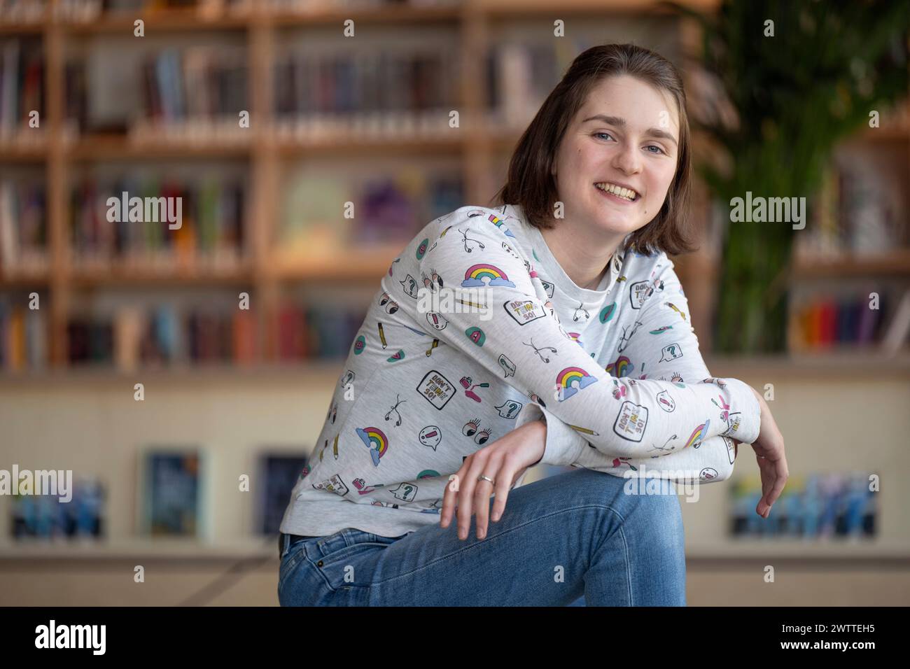 Persona sorridente in un maglione casual e jeans seduti in una biblioteca Foto Stock
