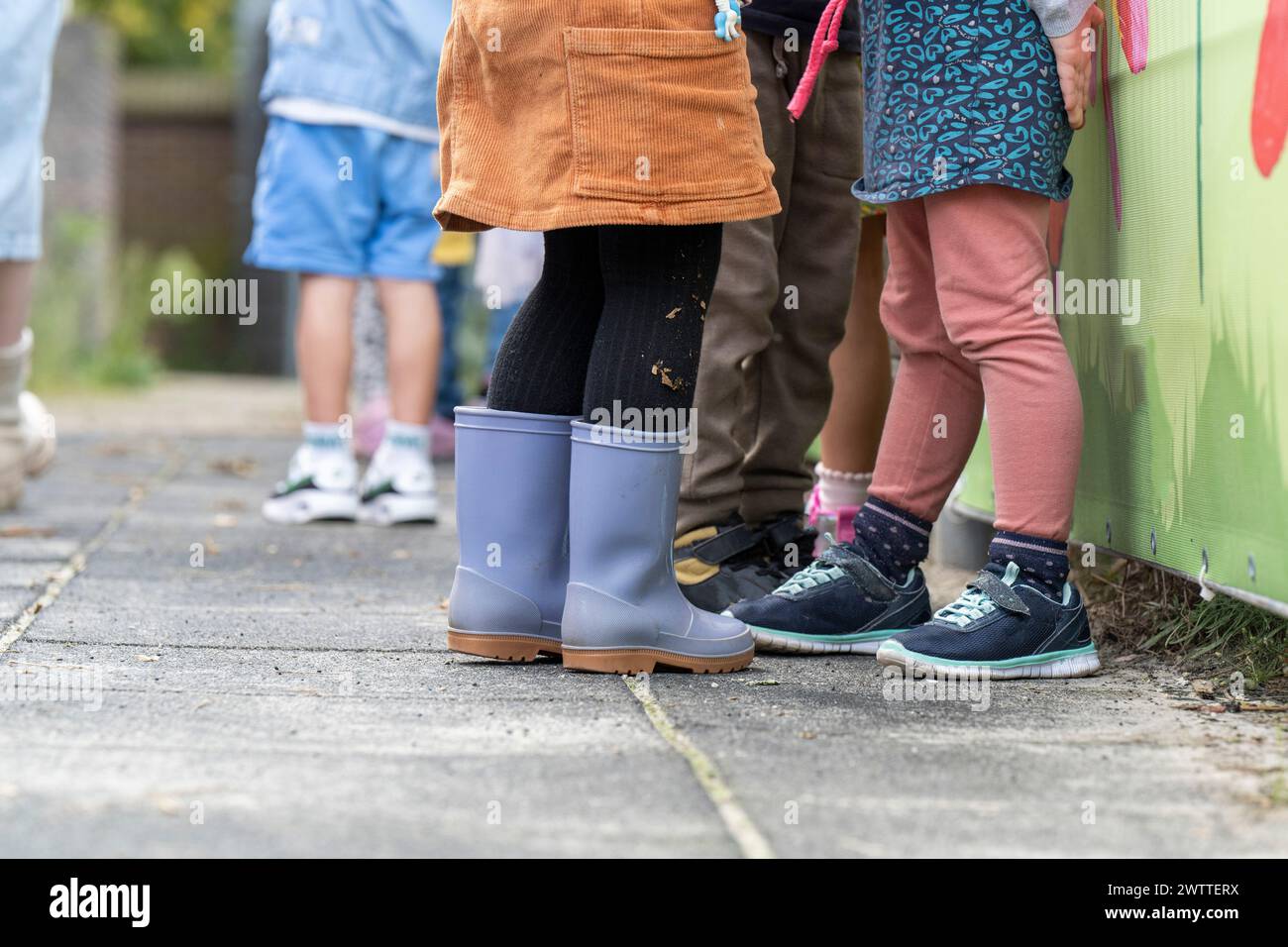 I bambini si sono schierati contro una recinzione colorata, con una varietà di calzature e abbigliamento giocoso. Foto Stock