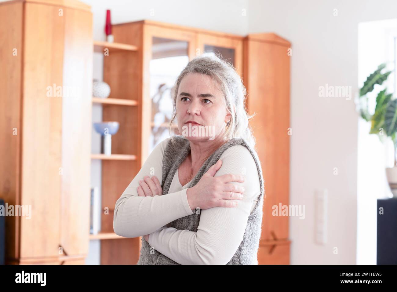 Una donna pensiva in piedi in casa con le braccia incrociate. Foto Stock