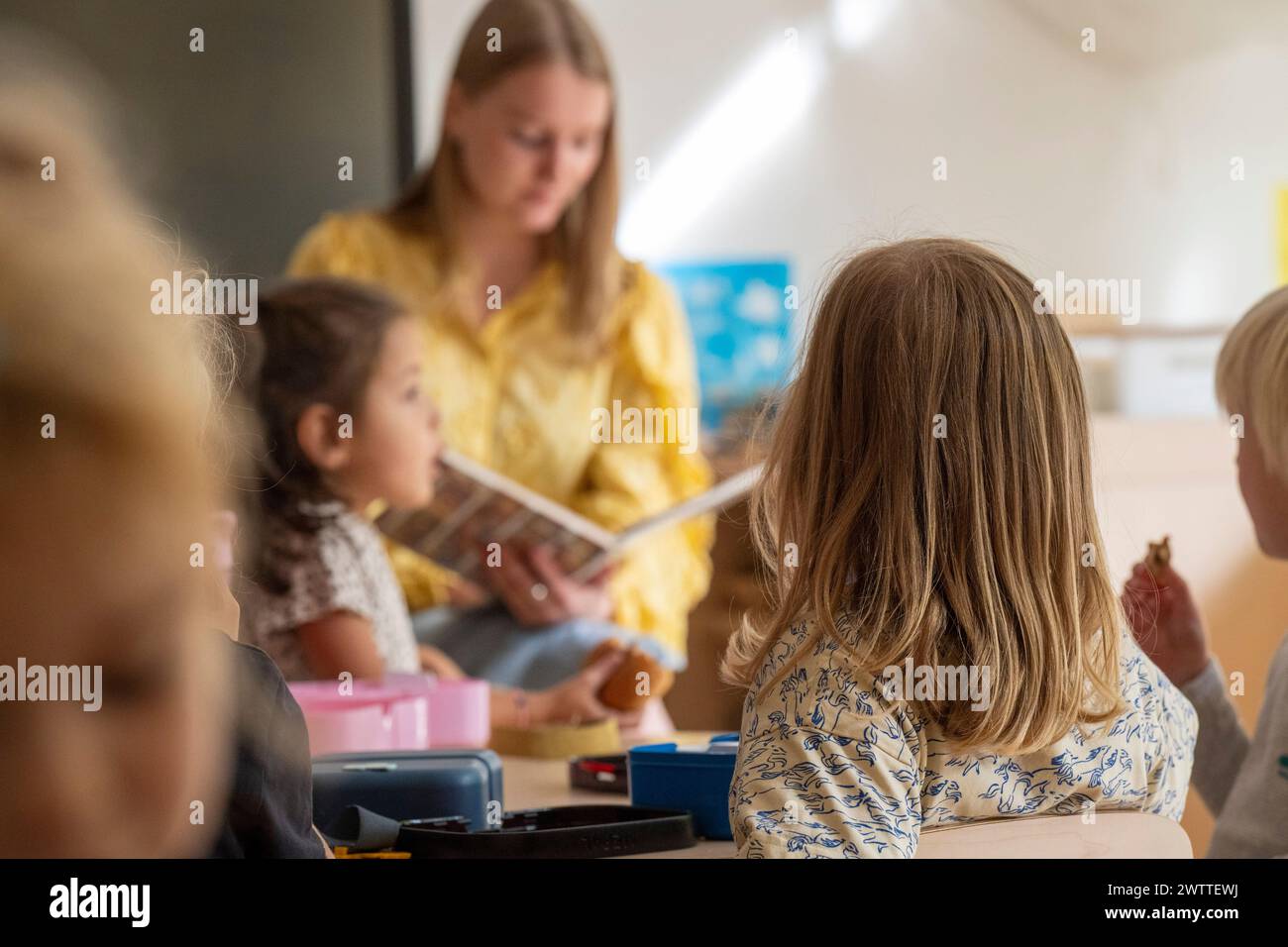 Un insegnante che si impegna con i giovani studenti durante la storia in un ambiente luminoso in classe. Foto Stock