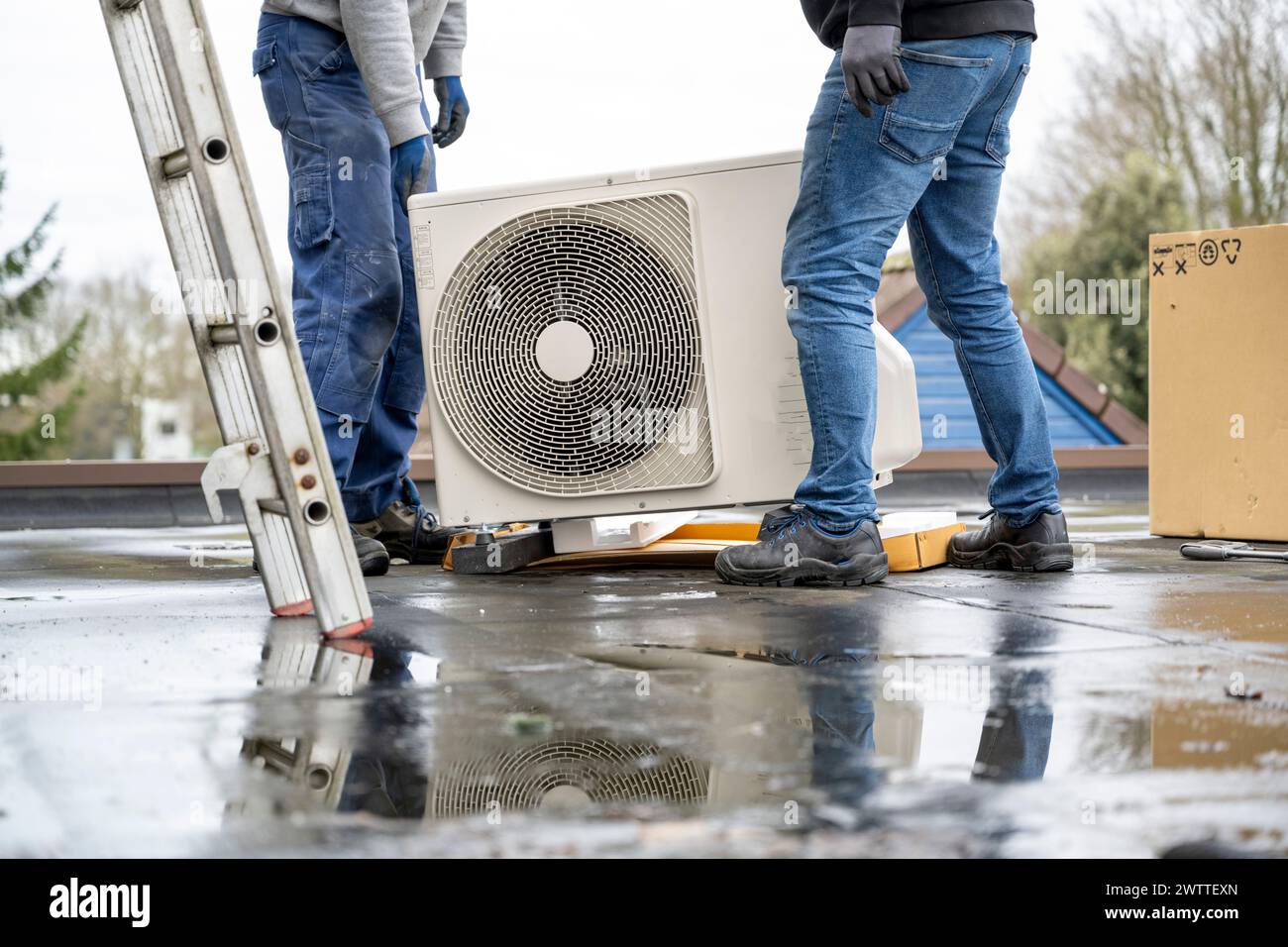 Due lavoratori che installano un impianto di aria condizionata su un tetto in una giornata nuvolosa. Foto Stock