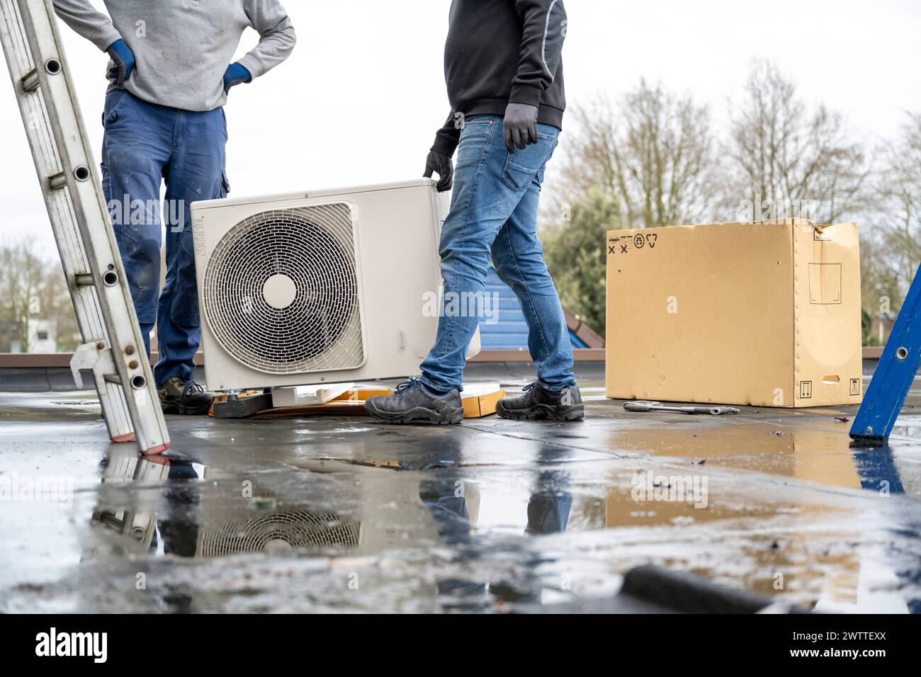 Due lavoratori che installano un impianto di aria condizionata su un tetto in una giornata nuvolosa. Foto Stock