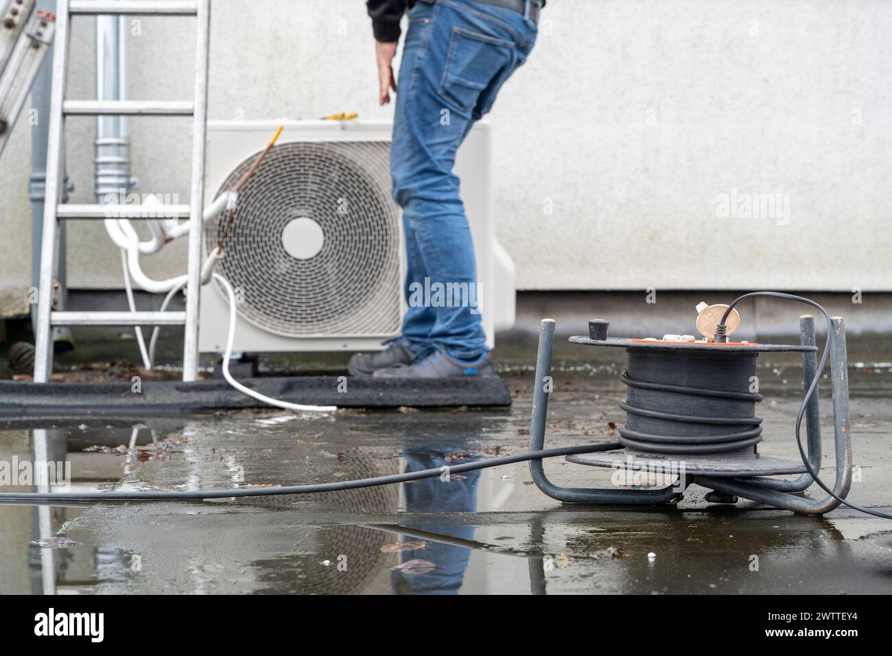 Persona che esegue la manutenzione di un'unità HVAC esterna su un tetto bagnato. Foto Stock
