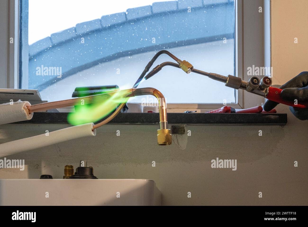 Le scintille volano mentre un professionista lavora su impianti idraulici sotto una finestra luminosa. Foto Stock