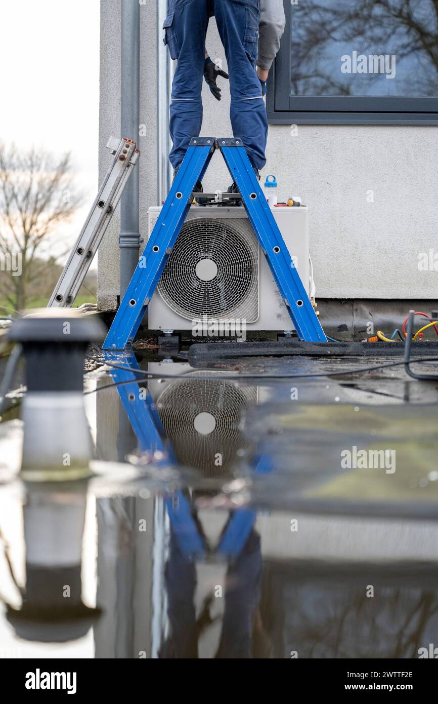 Un tecnico lavora su un'unità HVAC esterna, in piedi su una scala blu. Foto Stock