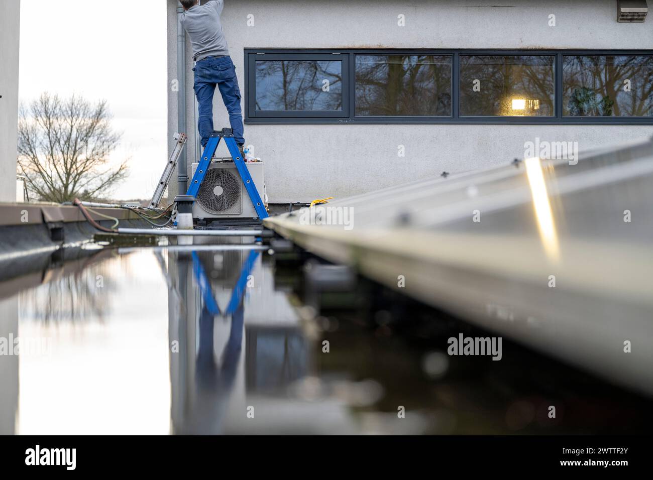 Tuttofare su una scala contro un edificio moderno, con un riflesso nell'acqua Foto Stock