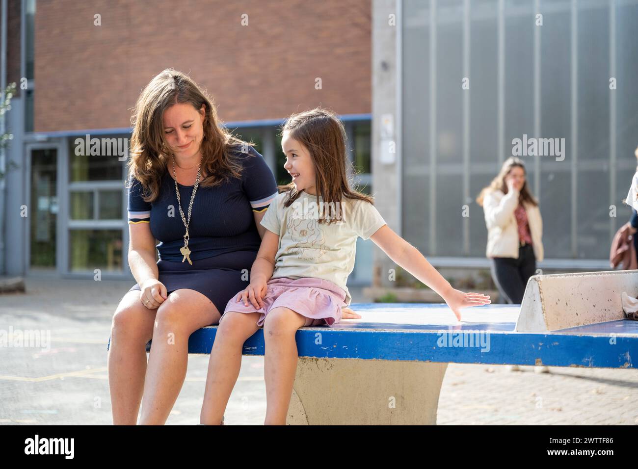 Una conversazione allegra tra una giovane ragazza e una donna seduta fuori in una giornata di sole. Foto Stock