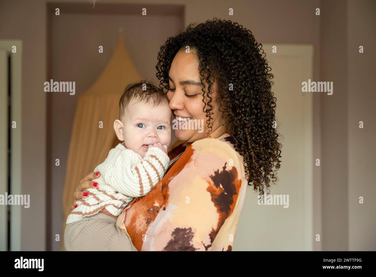 Una madre amorevole che tiene il bambino vicino con un sorriso caldo. Foto Stock