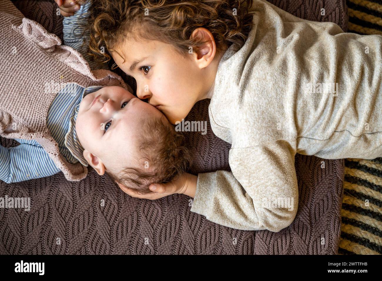 Un fratello più anziano dà un aspetto tenero a uno più giovane sdraiato su una coperta accogliente. Foto Stock