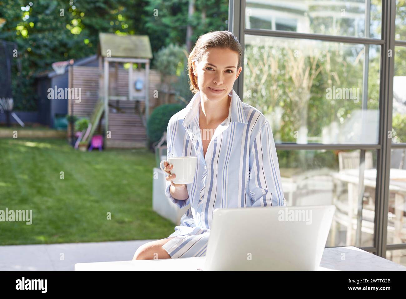 Donna con caffè e notebook in un cortile soleggiato Foto Stock