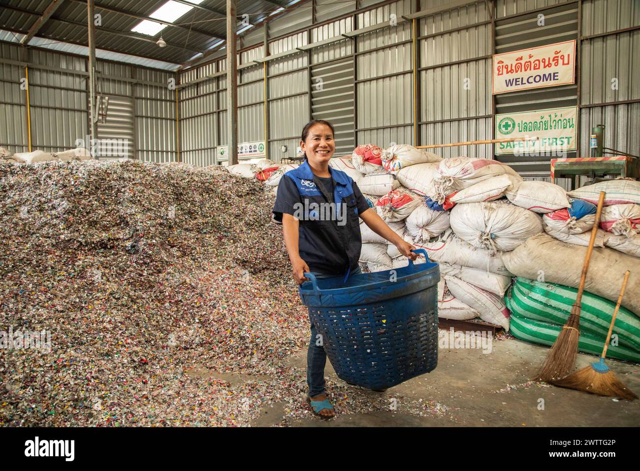 Lavoratore sorridente in mezzo a una montagna di tappi per bottiglie di plastica da riciclare, fabbrica di riciclaggio di plastica, Thailandia Foto Stock