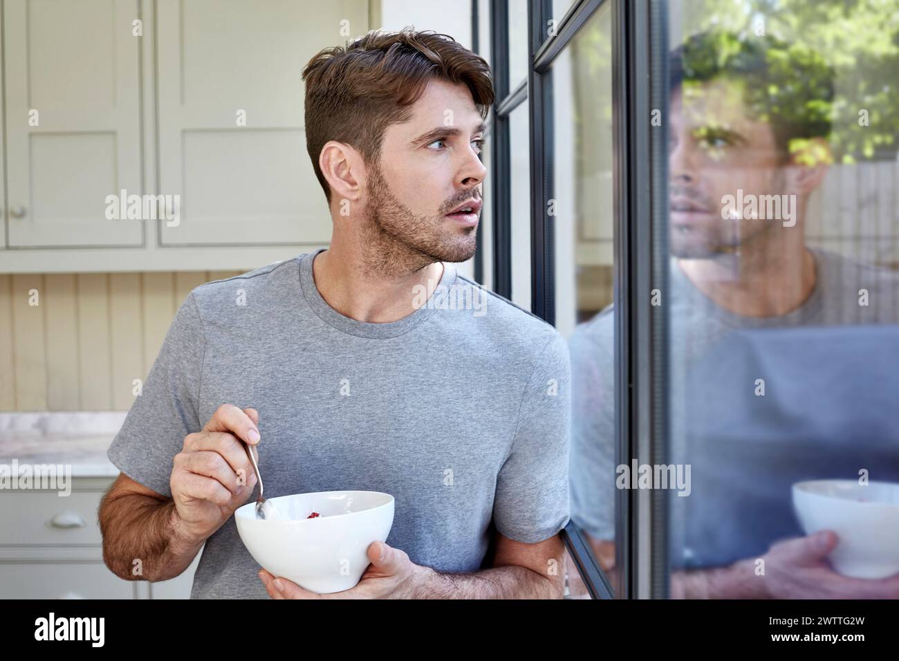 Uomo che mangia mentre guarda fuori dalla finestra Foto Stock