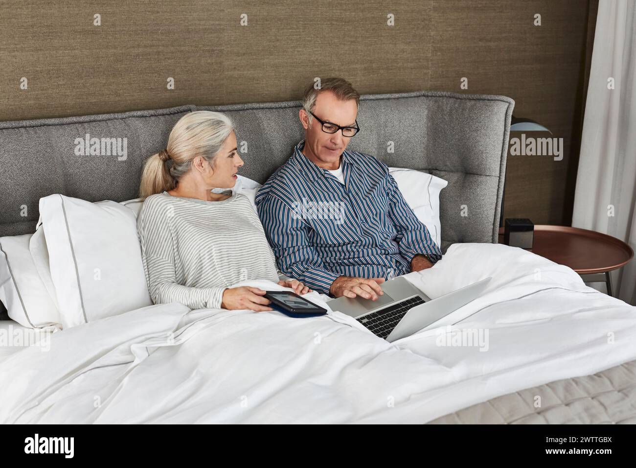 Coppia rilassante con un laptop e uno smartphone a letto Foto Stock