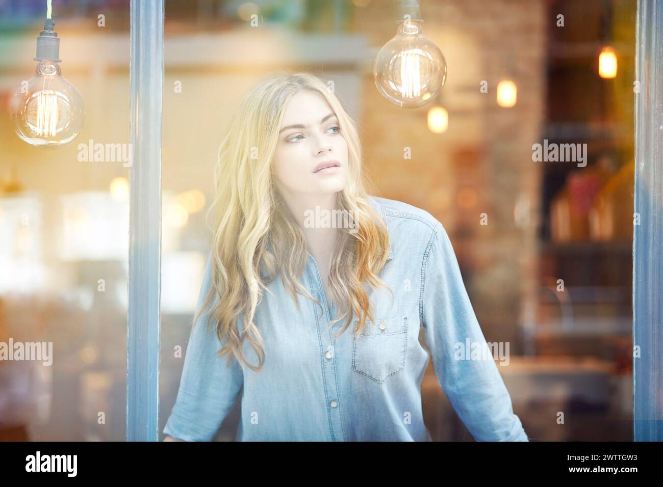 Donna che guarda fuori da una finestra con le lampadine. Foto Stock