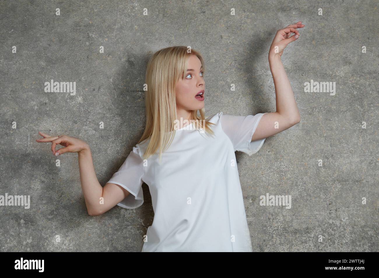 Donna che posa con espressione sorpresa contro un muro grigio Foto Stock