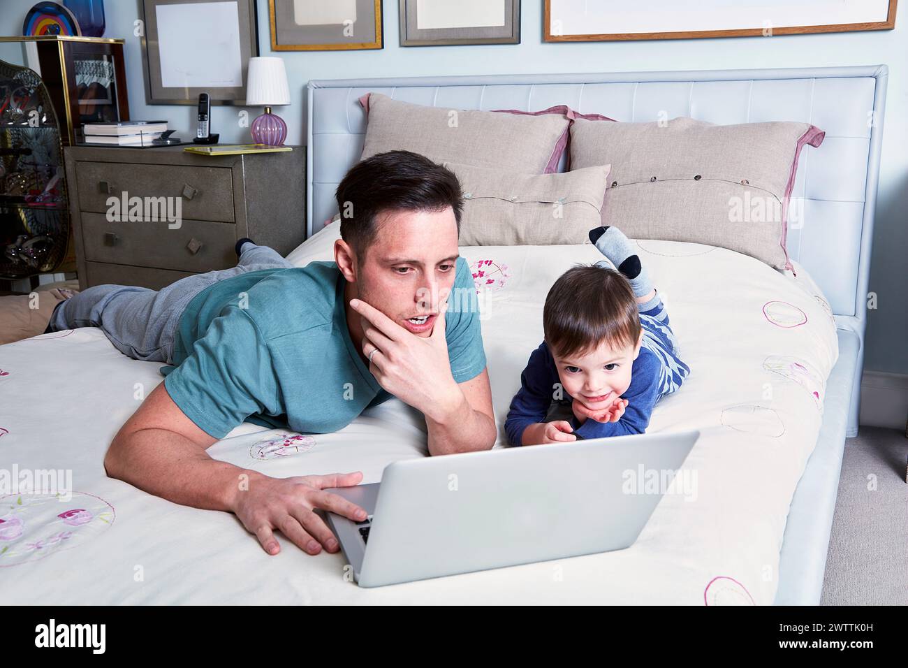 Uomo e bambino che usano un computer portatile a letto Foto Stock
