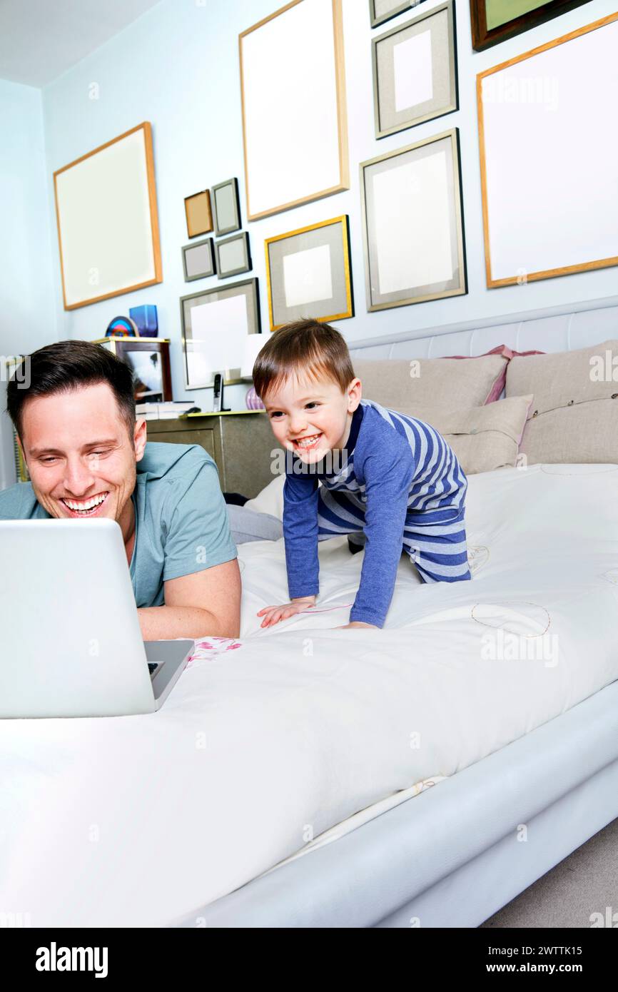 Uomo e bambino sorridono al laptop su un letto Foto Stock