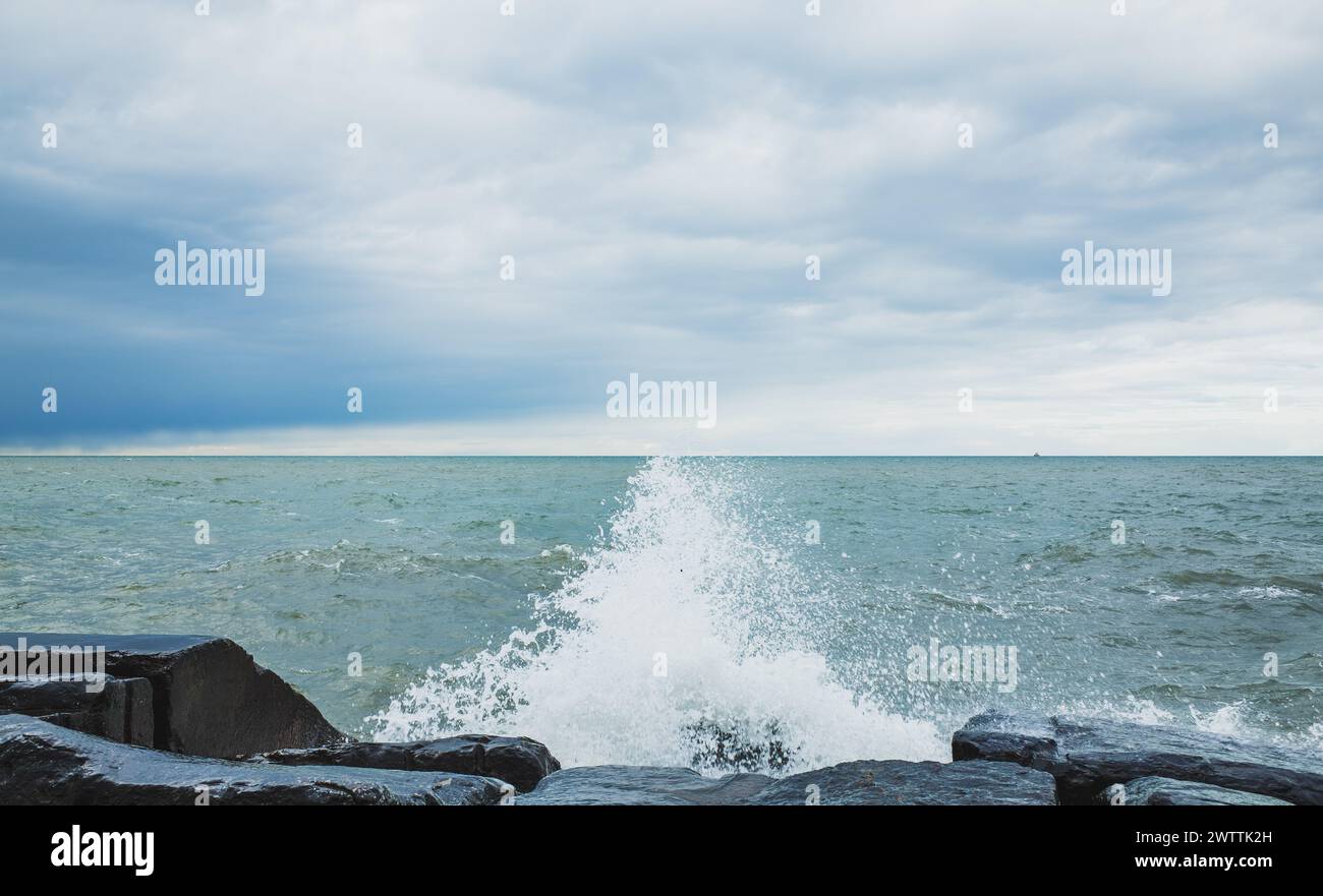Le tempeste onde oceaniche si schiantano contro la costa rocciosa frastagliata sotto il cielo nuvoloso Foto Stock