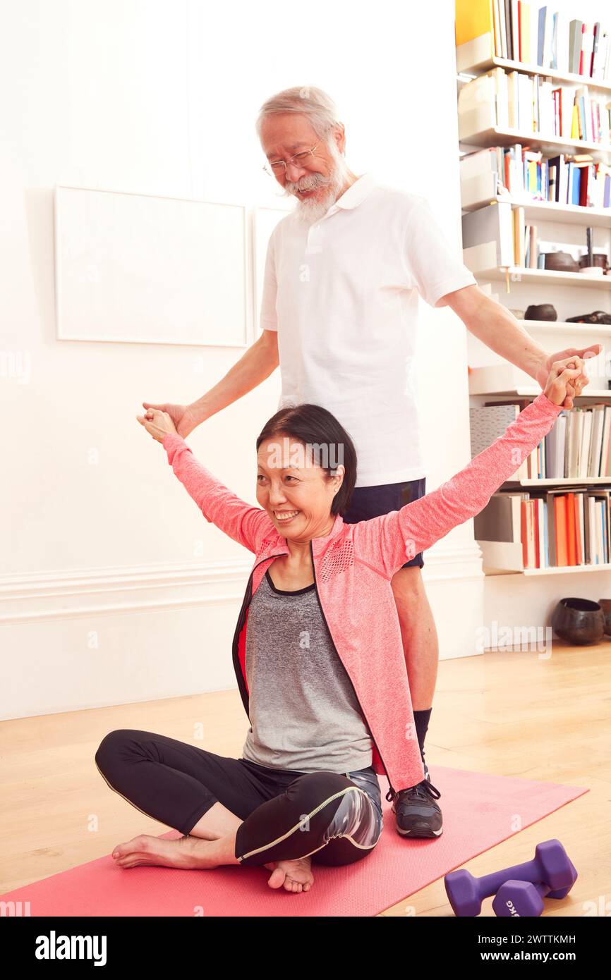 Uomo anziano che assiste una donna in una posa yoga Foto Stock