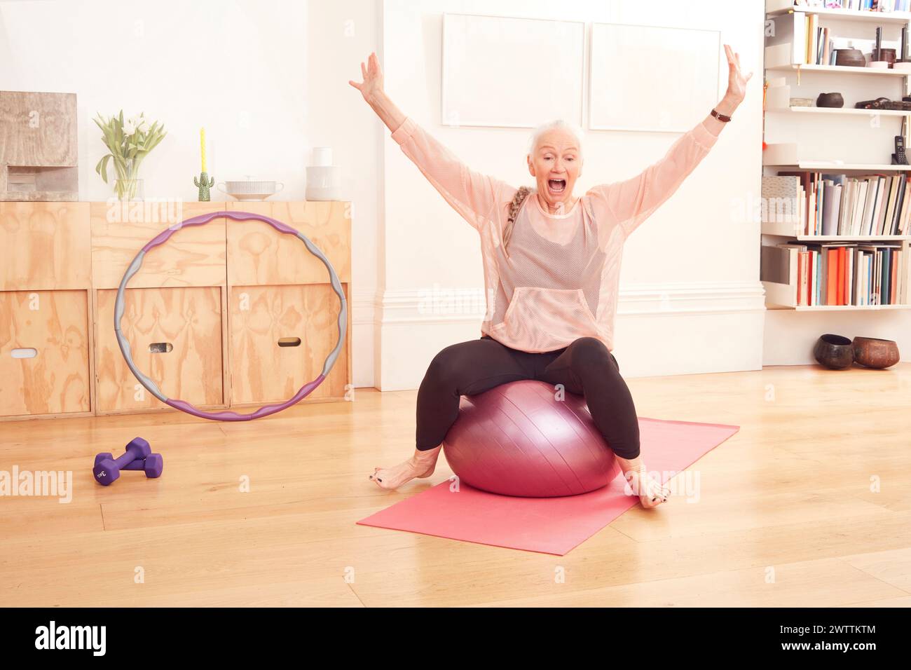 Donna anziana che si allena con una palla fitness a casa. Foto Stock