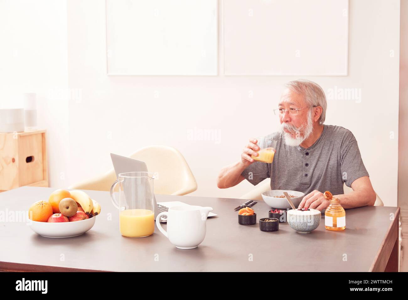 Un anziano che fa colazione e usa un notebook Foto Stock