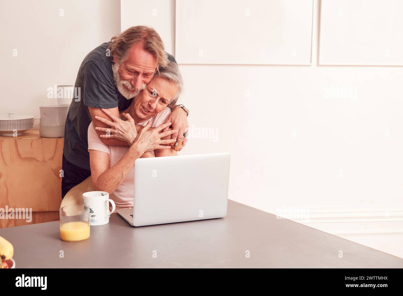 Una coppia di anziani che si abbraccia mentre utilizza un notebook a casa. Foto Stock
