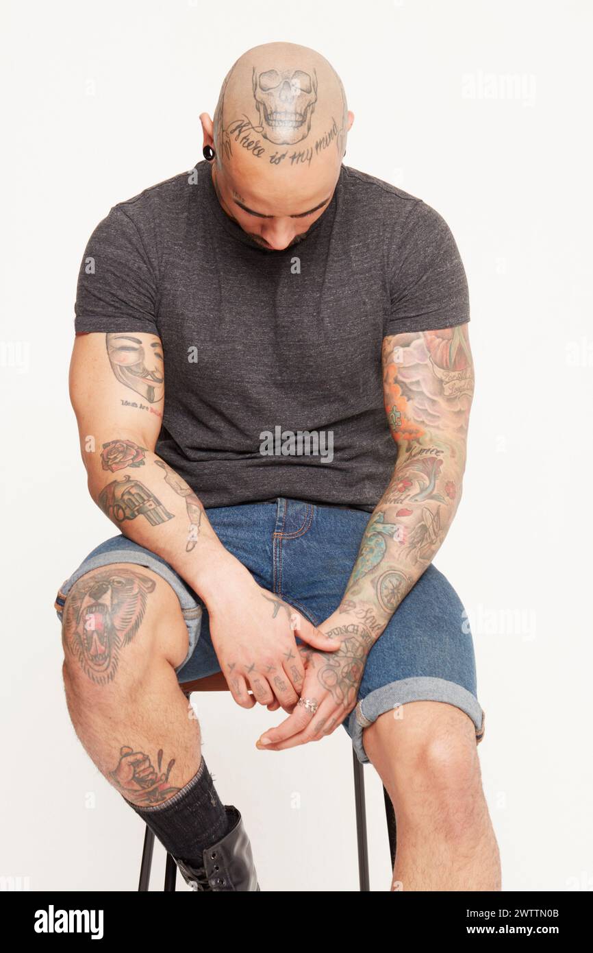 Uomo con tatuaggi seduto su uno sgabello Foto Stock