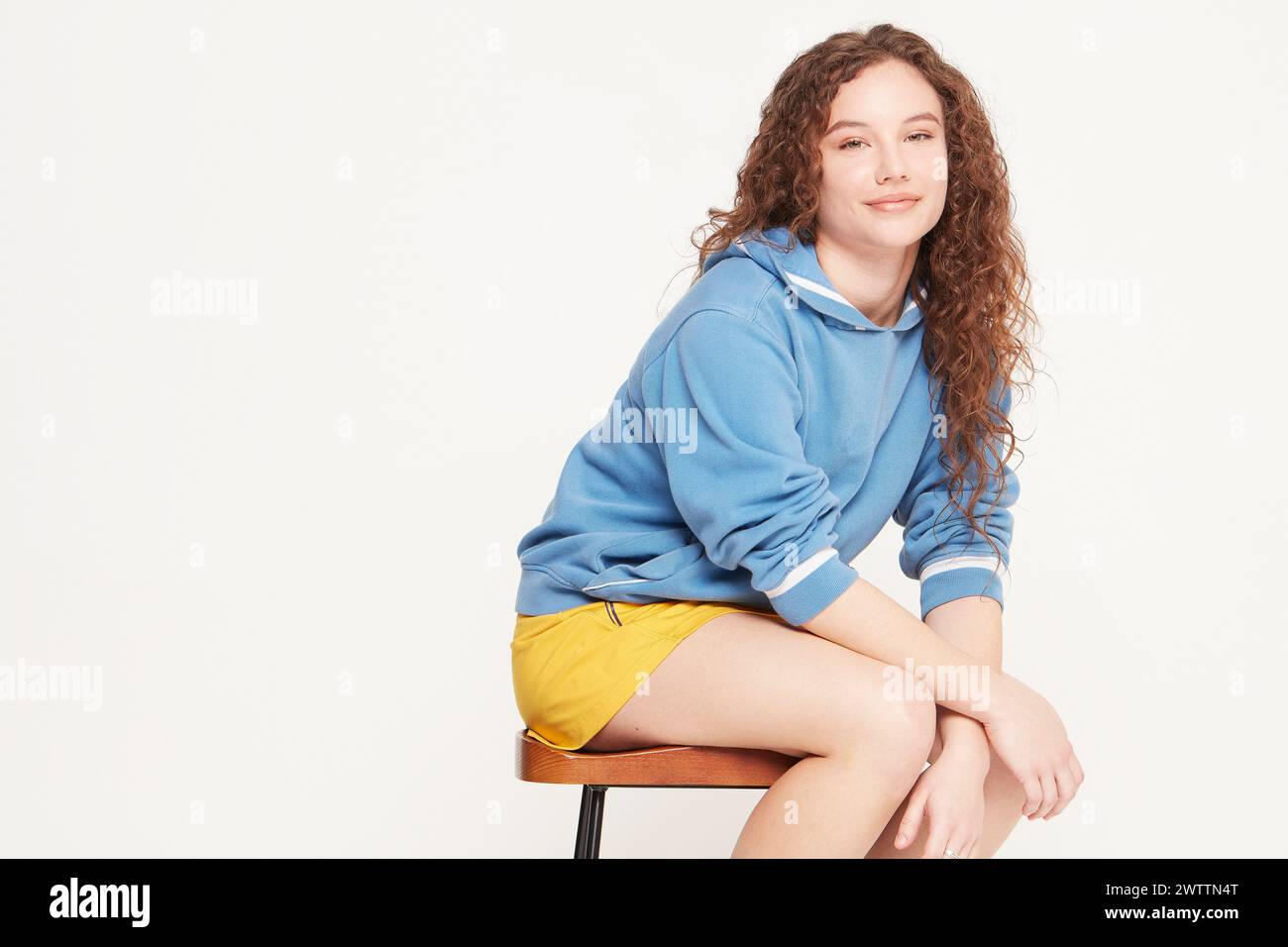 Donna seduta su uno sgabello con felpa blu e pantaloncini gialli Foto Stock