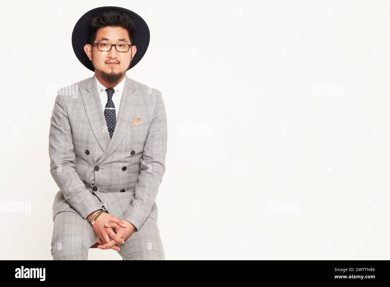 Uomo con vestito grigio e cappello nero seduto Foto Stock