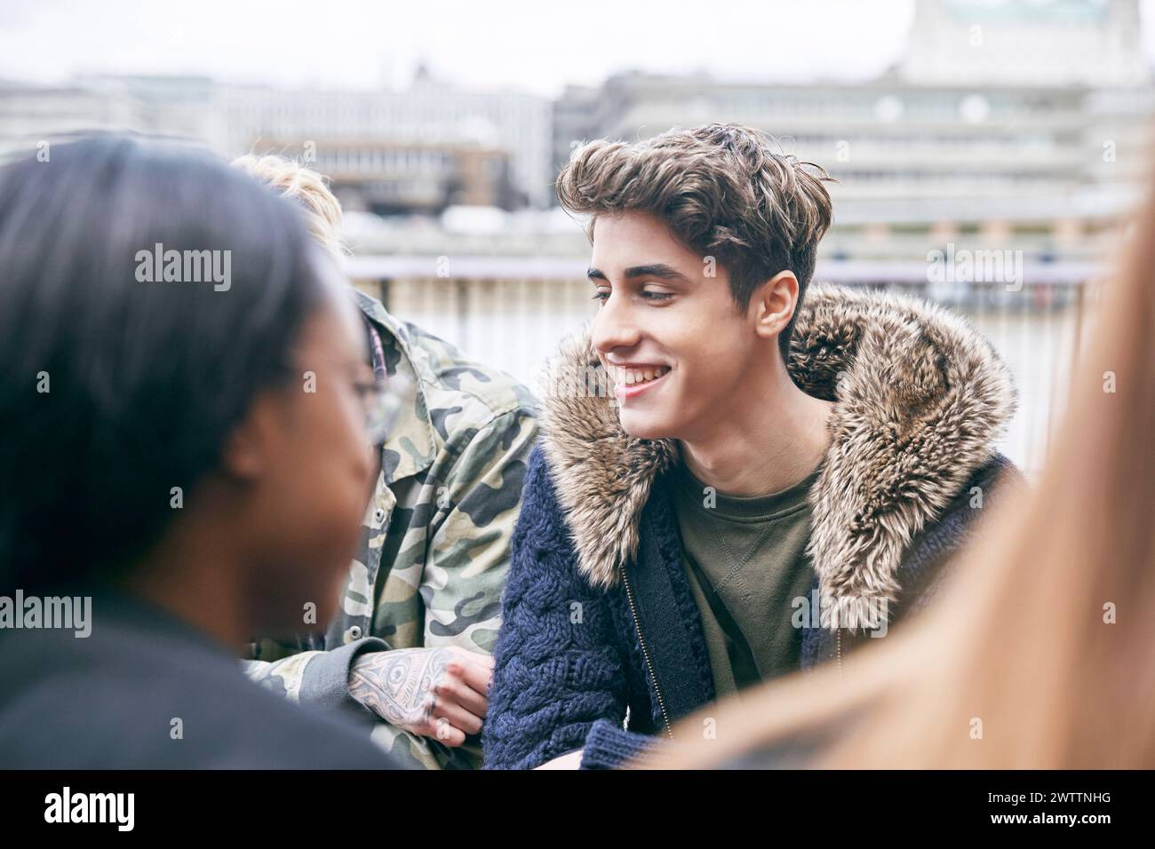 Adolescente sorridente in una giacca con cappuccio in pelliccia che parla con gli amici Foto Stock