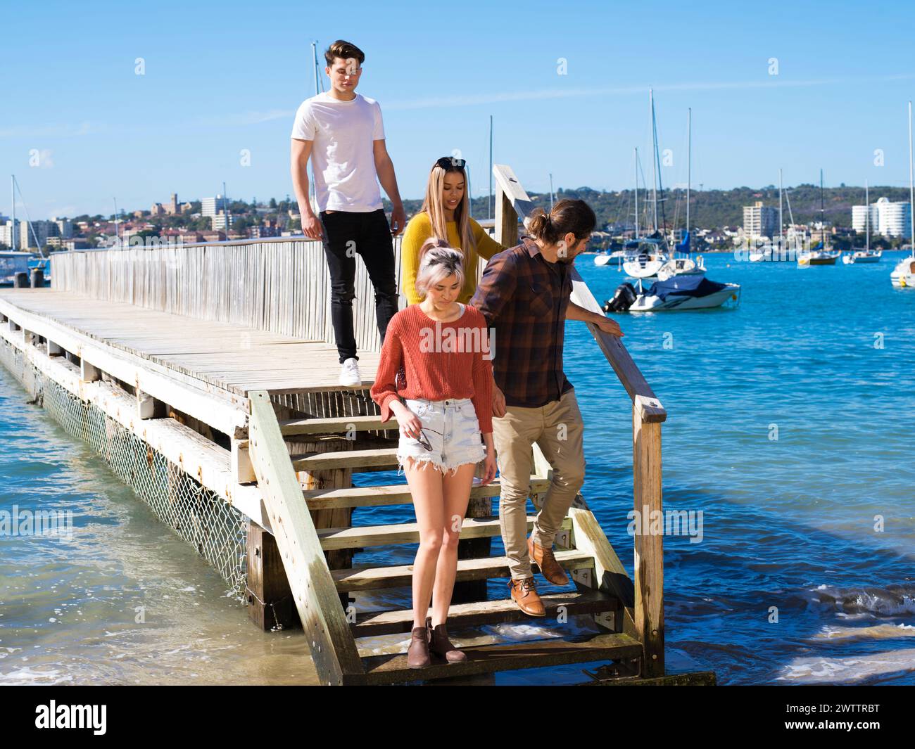 Gruppo di amici che si godono una giornata di sole su un molo di legno vicino al mare Foto Stock