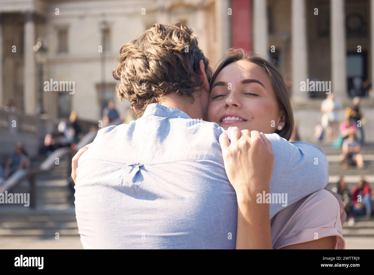 Coppia che abbraccia in una piazza pubblica soleggiata Foto Stock