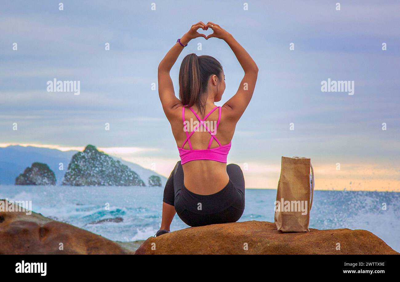 Donna che fa forma al cuore con le mani in spiaggia Foto Stock