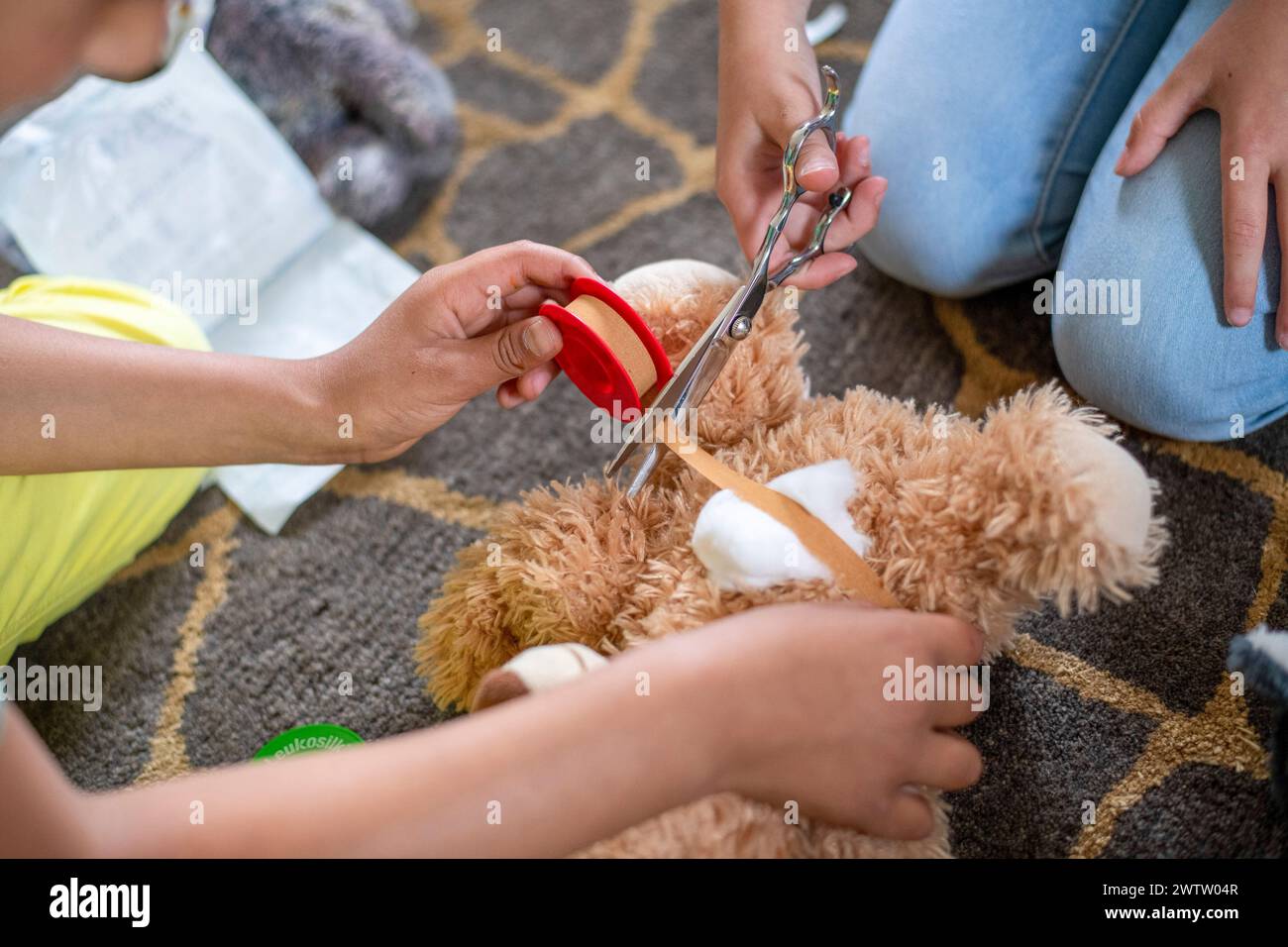Giocare con il medico le mani di Un bambino usando le forbici giocattolo su un orsacchiotto mentre gli altri lo guardano. Foto Stock