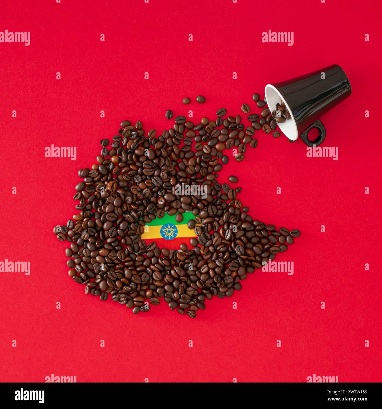 Composizione creativa realizzata con tazza di caffè, mappa dell'Etiopia realizzata con chicchi di caffè tostati e bandiera etiope su sfondo rosso. Layout minimo. Foto Stock