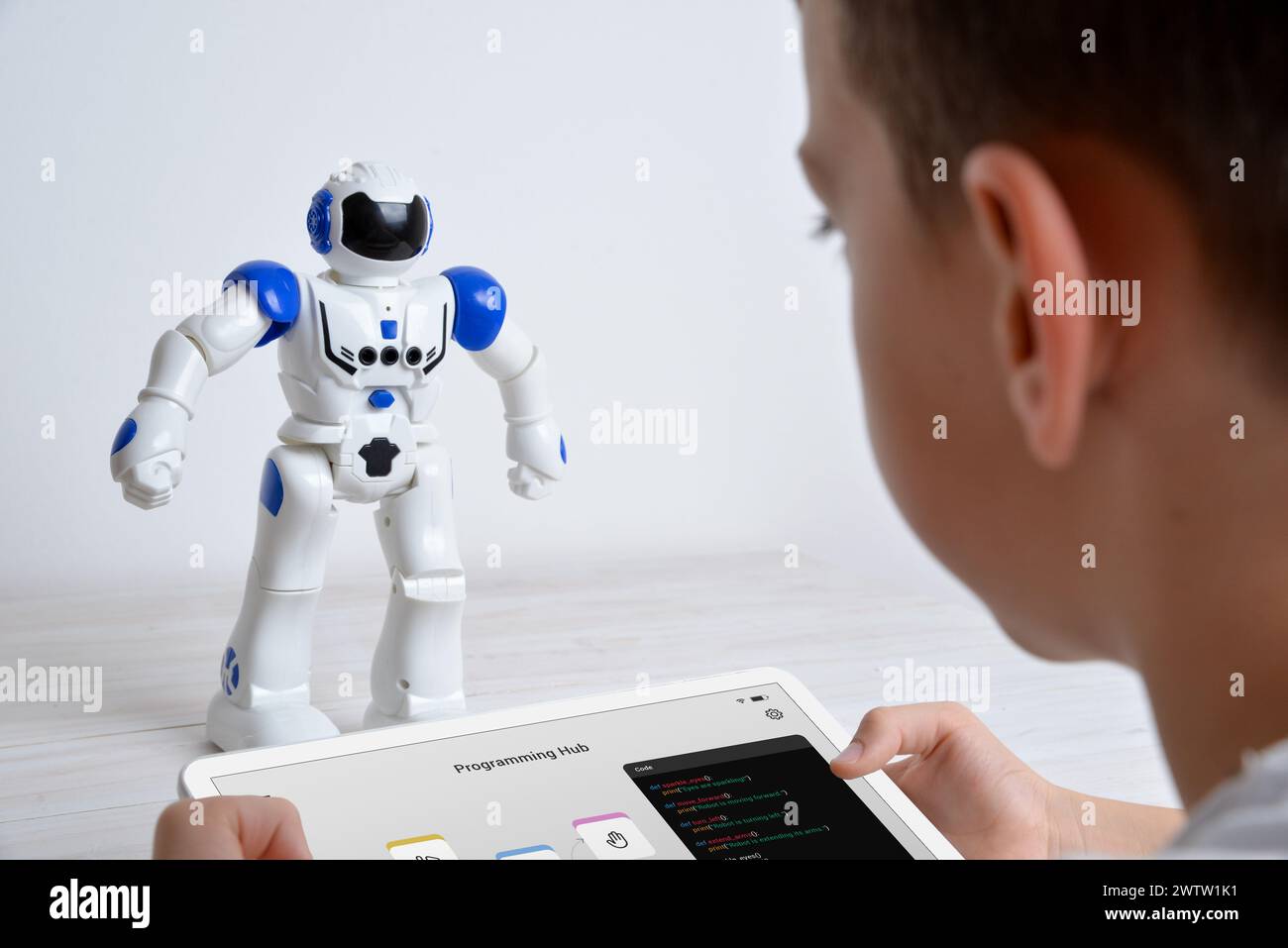 Il ragazzo controlla il robot utilizzando un tablet sulla scrivania. Illustrando esperienze didattiche, tecnologiche, innovative e di apprendimento interattivo in robotica e programmazione Foto Stock
