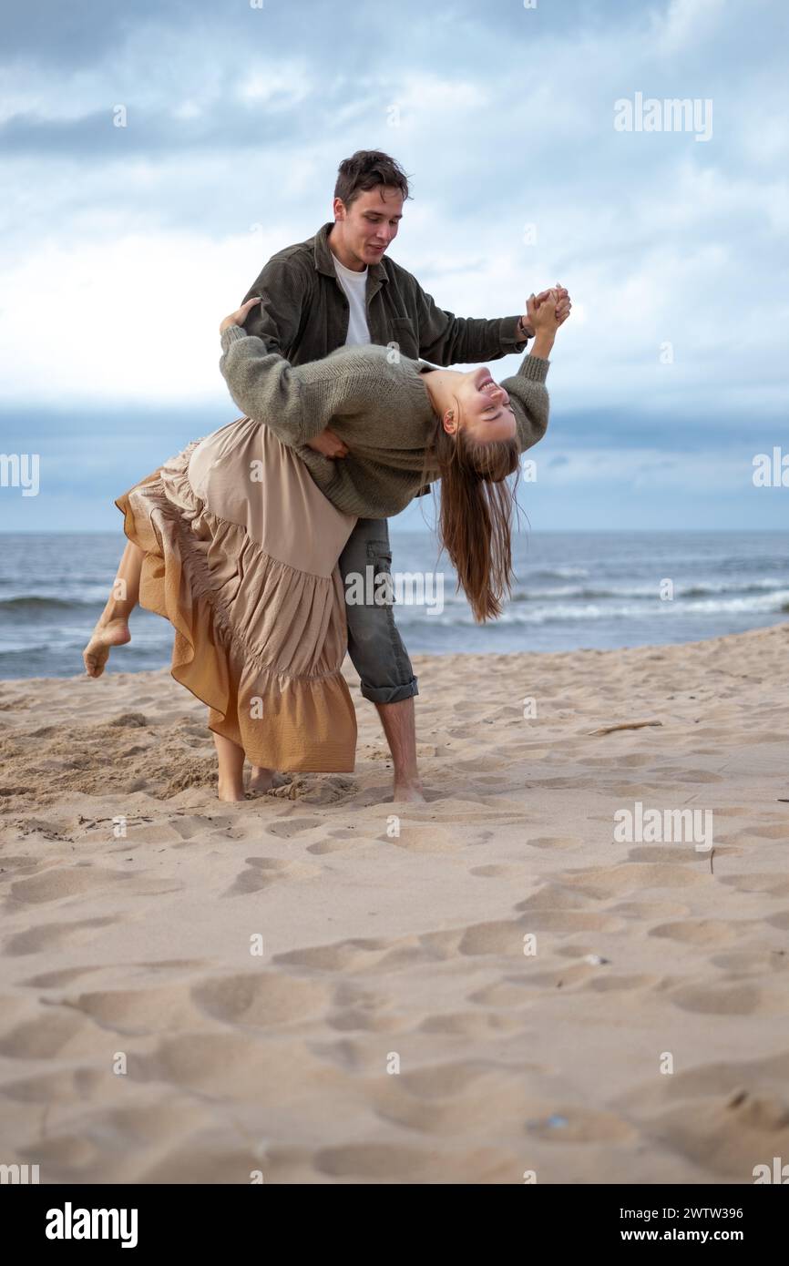 Uomo che gira una donna in un abito fluente sulla spiaggia, sia in mezzo alla risata, una danza diserbante o di fidanzamento. Un momento vivace e gioioso, perfetto per lo stile di vita Foto Stock