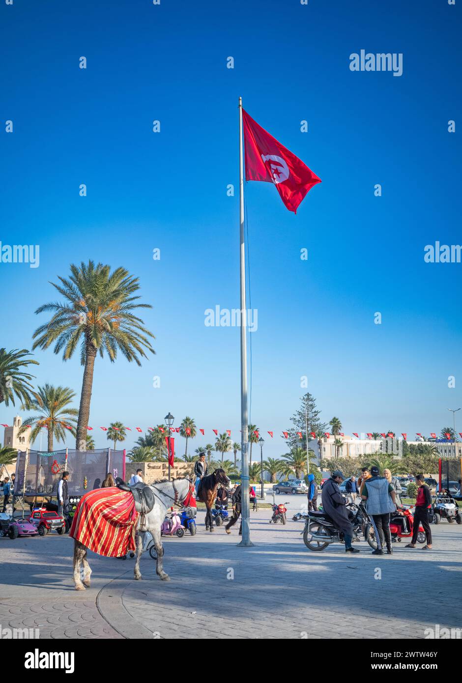 Un cavallo attende i turisti mentre le persone si incontrano e parlano accanto a una bandiera tunisina in piazza Bourguiba, Monastir, Tunisia. Foto Stock