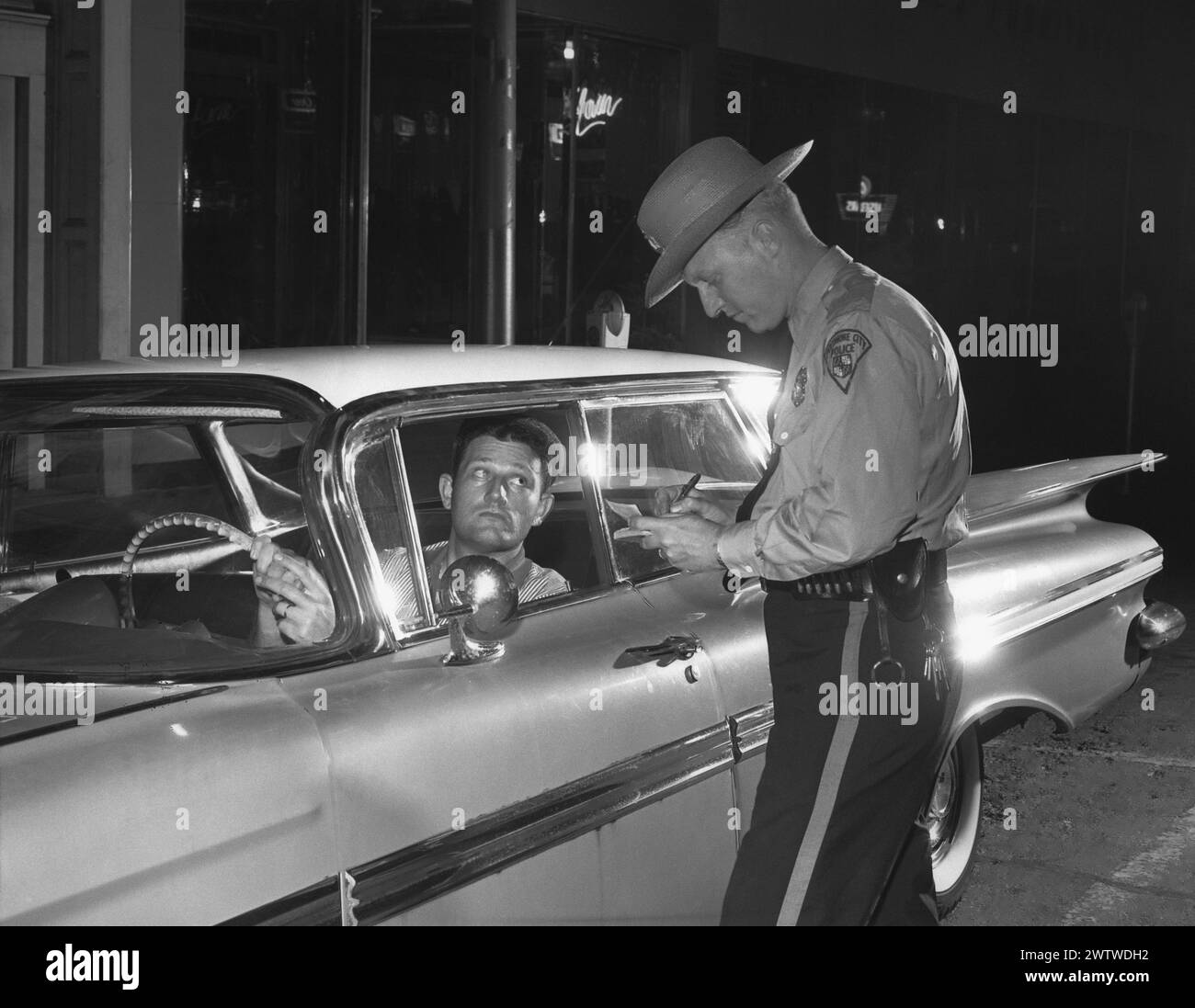 Un poliziotto scrive una citazione a un pilota maschio mentre si trova accanto alla sua Chevy Impala del 1957 Foto Stock