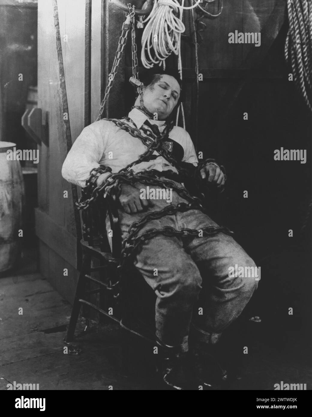 L'artista della fuga, Harry Houdini, fugge da una delle sue catene e da una corda senza alcun aiuto in una stanza buia, con una vista completa del pubblico Foto Stock