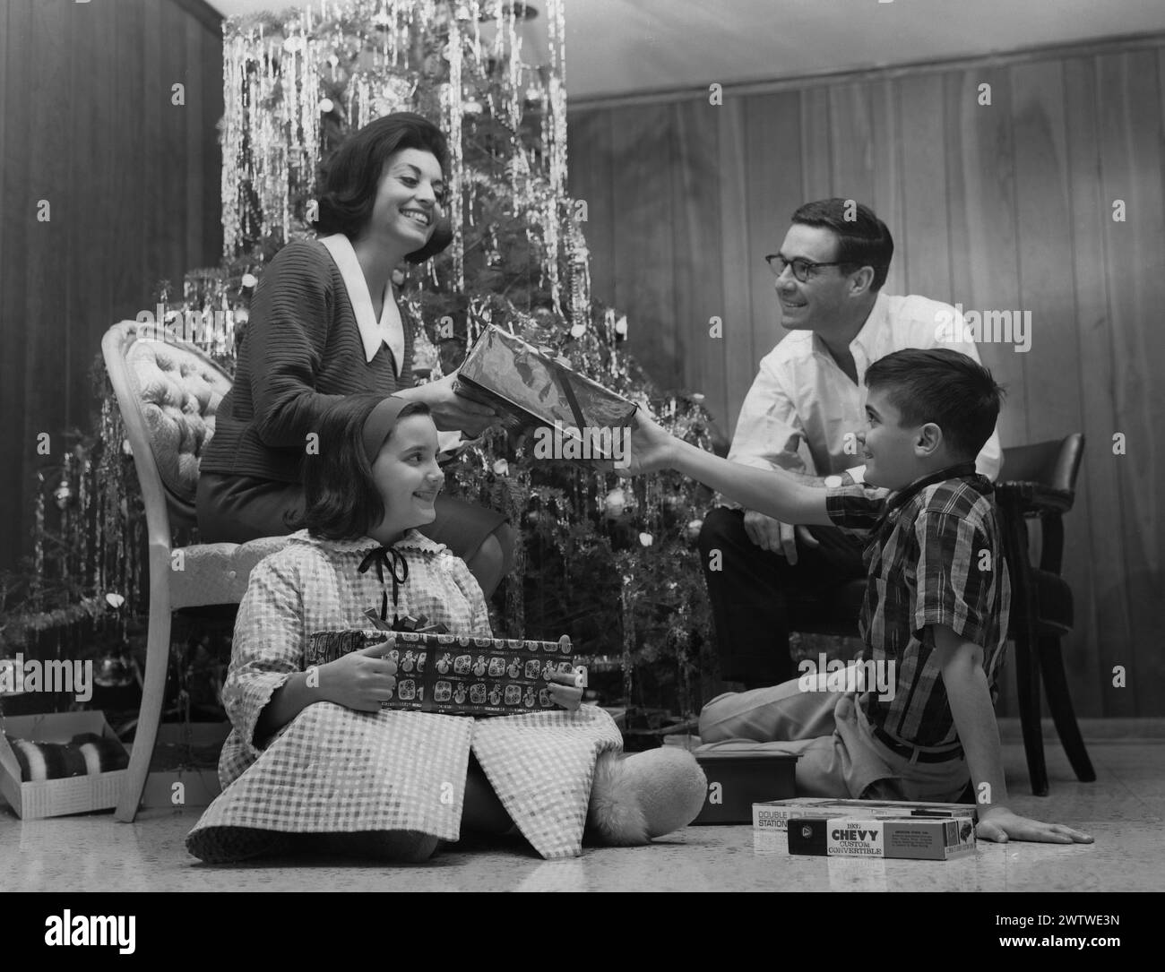 La famiglia è seduta di fronte a un albero di Natale decorato scambiando regali di Natale Foto Stock